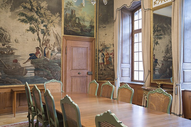Ein kleines Zimmer.  Im Vordergrund ein Holztisch mit mehreren Stühlen. Die Wände im Hintergrund sind vollständig mit Gemälden verkleidet.